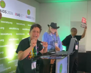 Asia Russell addresses speakers at the AIDS 2026 Conference during a protest. Other protesters are on stage with her.