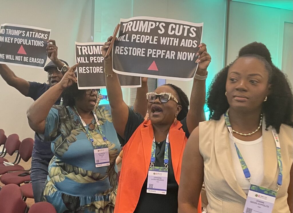 Four Black people at a protest at the AIDS 2026 conference. One holds a sign that says, "End Trump's attacks on key populations. We will not be erased." Two hold signs that say, "Trump's cuts kill people with AIDS. Restore PEPFAR now." The three people holding signs are also shouting or chanting.